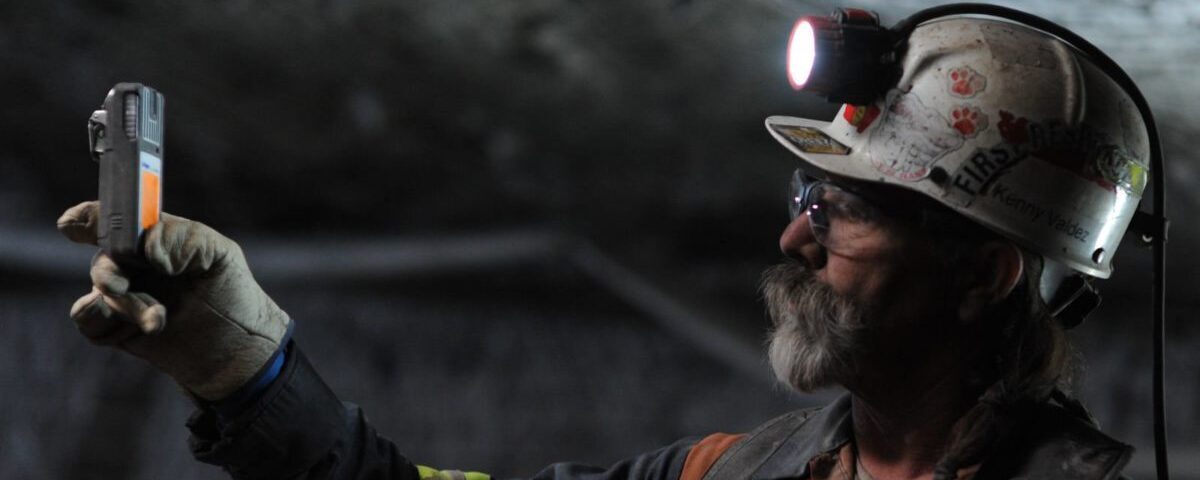 Արդյունաբերական աշխատող գլխակապով և անվտանգության սաղավարտով՝ օգտագործում ձեռնակ ստուգման սարքավորում մութ արդյունաբերական միջավայրում: