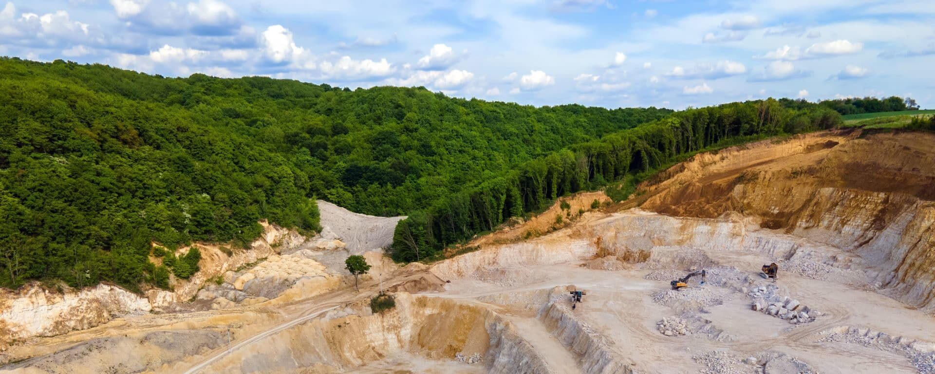 Մեծ բաց հանքահոր աստիճանակարգված լեռնահանքային մակարդակներով և ծանր տեխնիկայով՝ քար կամ հանքանյութեր արդյունահանելու համար, շրջապատված կանաچ անտառապատ բլուրներով: