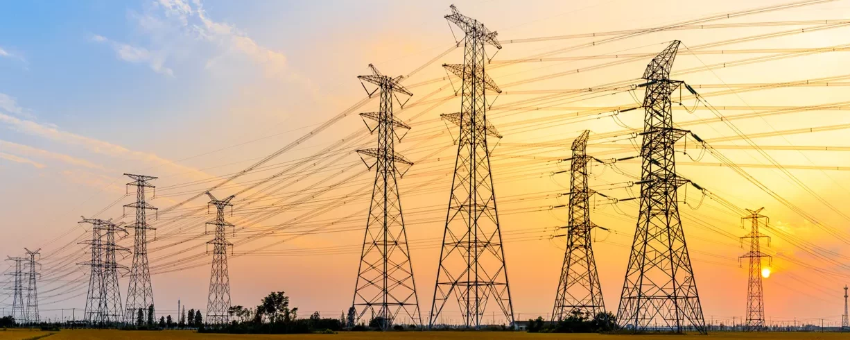 Բարձր լարման էլեկտրական փոխանցման աշտարակներ և էլեկտրական գծեր, որոնք տարածվում են լանդշաֆտի վրայով մայրամուտին, բազմաթիվ պողպատե վանդակային աշտարակներով, որոնք տանում են էլեկտրական մալուխներ ոսկեգույն երկնքի դեմ